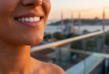 Eine Nahaufnahme eines perfekten, weißen Lächelns. Im unscharfen Hintergrund ist die malerische Skyline von Istanbul bei Sonnenuntergang zu sehen, was das Thema Zahntourismus in die Türkei visualisiert.