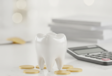 Eine Nahaufnahme eines stilisierten, gesunden Zahns auf einem hellen Schreibtisch, umgeben von unscharfen Münzen und einem nicht lesbaren Rechner, die die finanziellen Aspekte von Zahnbehandlungen und Krankenkassen-Erstattungen symbolisieren. Der Hintergrund ist weich gezeichnet, ohne sichtbaren Text.